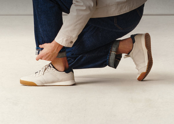 Person tying shoelaces on white sneakers with brown soles on a light background