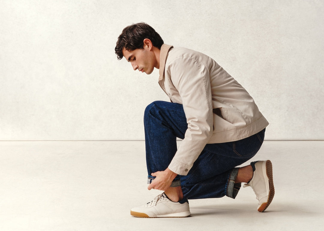 Man adjusting his white sneakers on a plain background