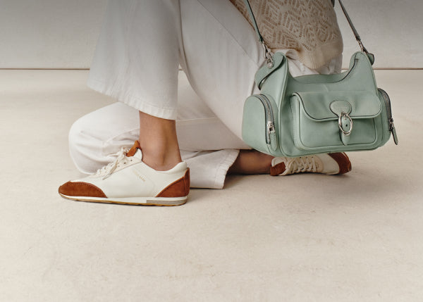 Person wearing white pants and brown and white sneakers, holding a light green handbag.