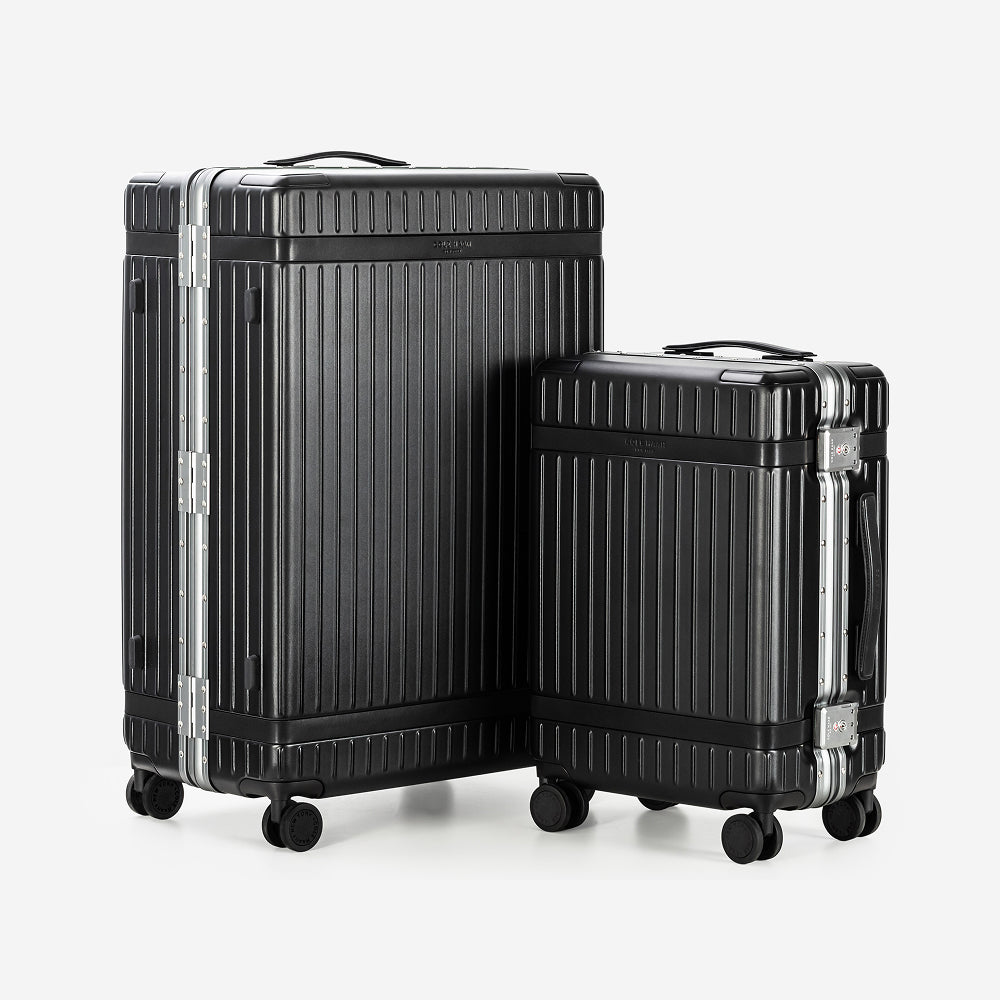 Two hard-shell spinner suitcases in black with silver aluminum trim, shown on a light gray background.