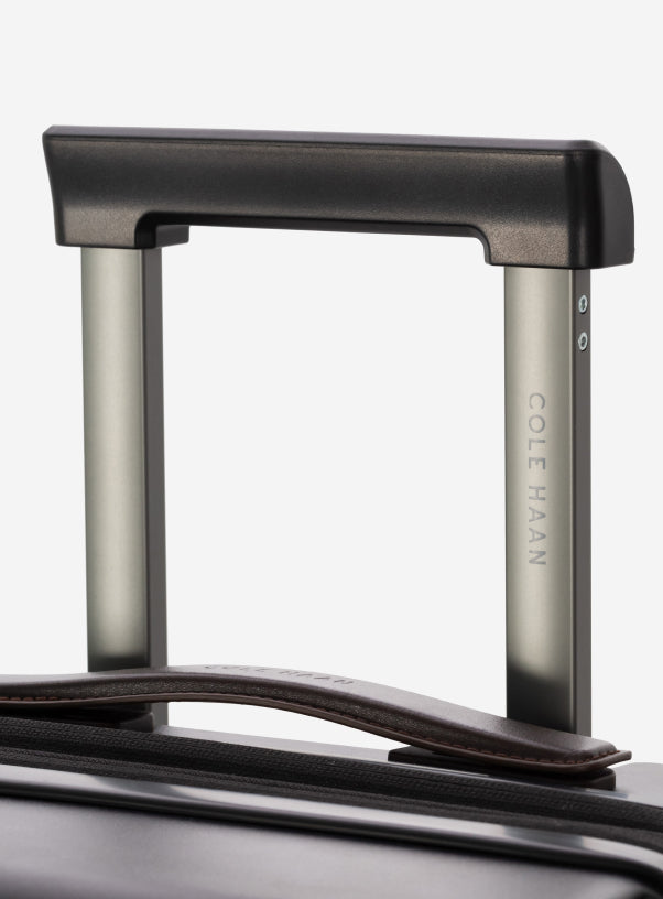 Close-up of a suitcase handle with 'Cole Haan' branding on a white background