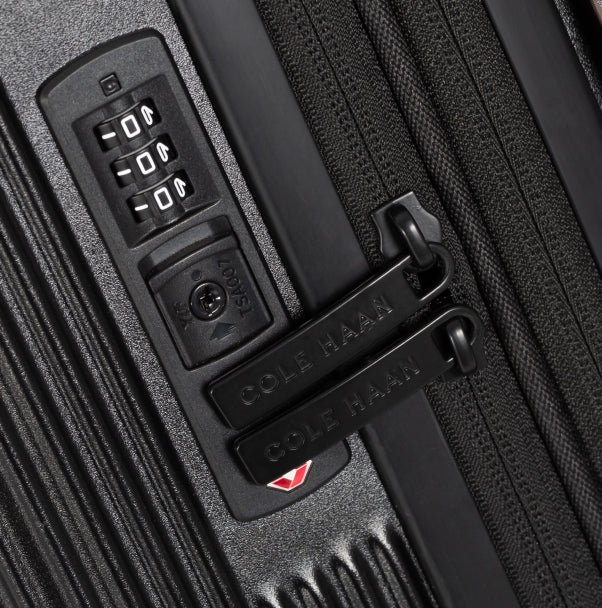 Close-up of a black suitcase handle with a combination lock and Cole Haan branding.