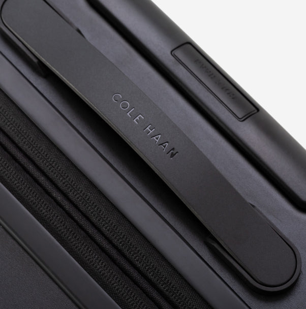 Close-up of a black suitcase with 'Cole Haan' branding on a white background