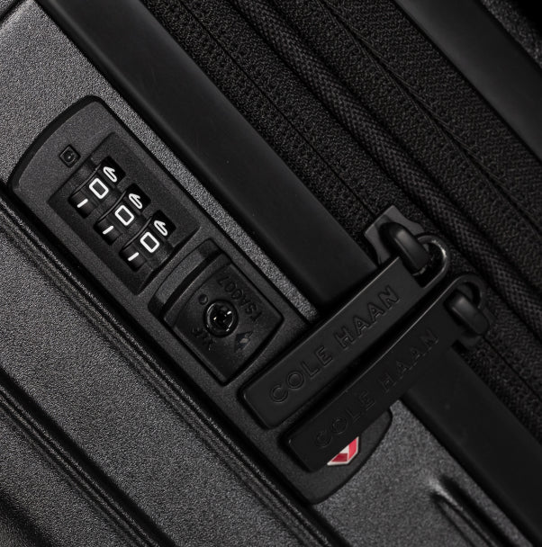 Close-up of a black suitcase with a combination lock and Cole Haan branding.