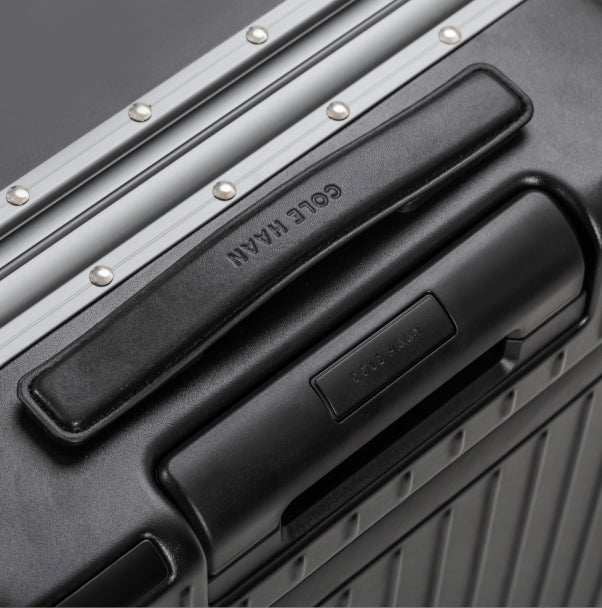 Close-up of a black suitcase handle with 'Gole Han' branding on a metallic surface.