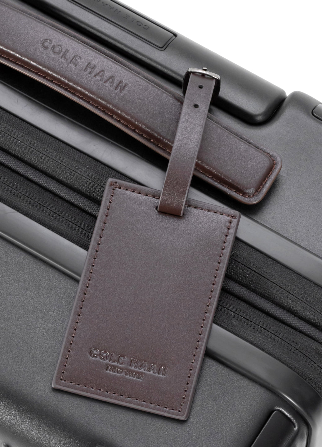 Black suitcase with a brown leather tag featuring 'Cole Haan' branding.
