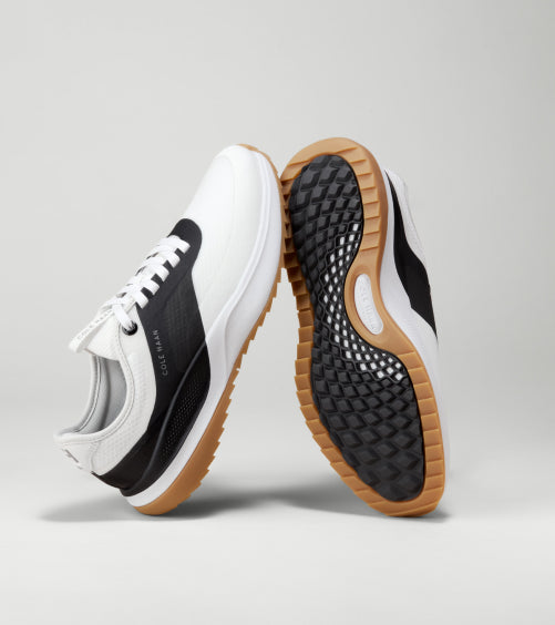 White and black golf shoes with brown soles on a light gray background