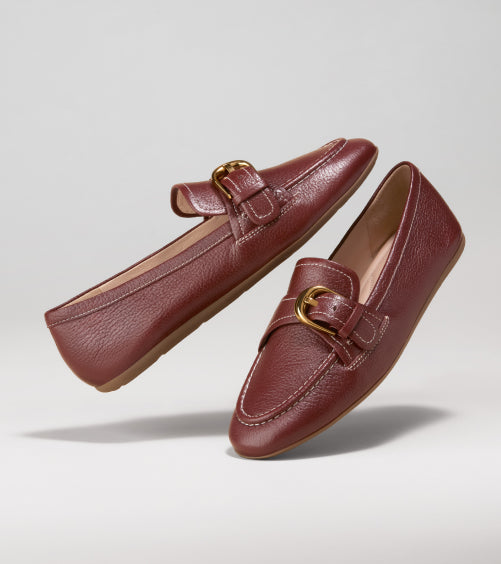 Pair of brown loafers with gold buckles on a light gray background