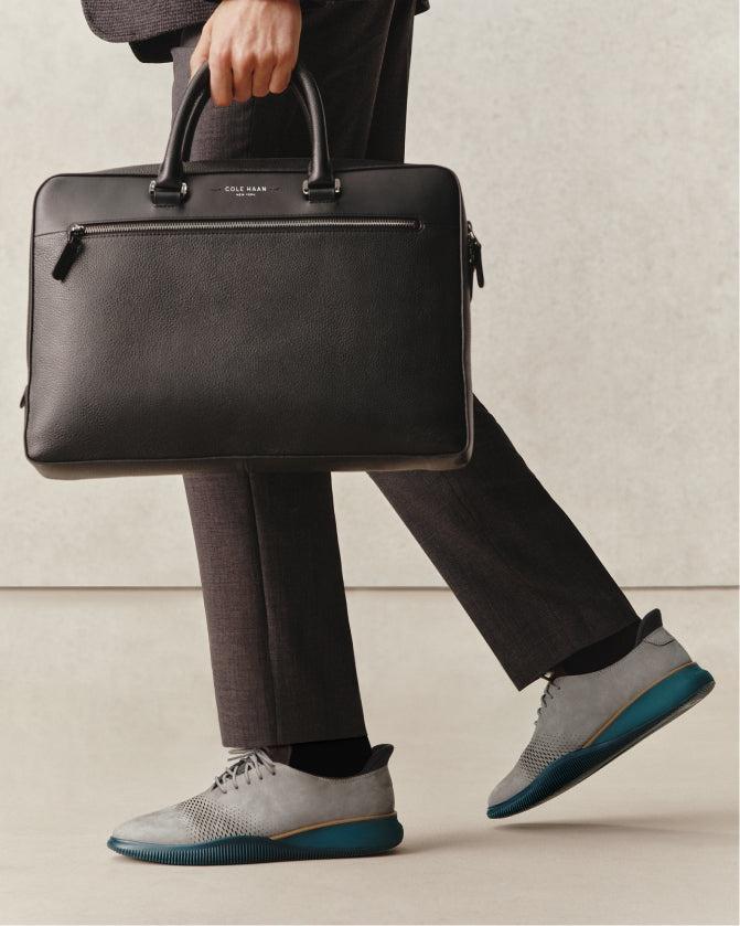 Person holding a black leather briefcase with a neutral background