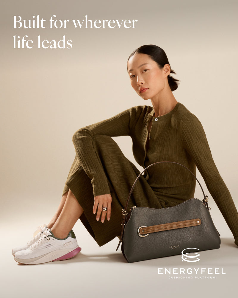 A woman sits on a beige floor wearing an olive green ribbed knit cardigan and matching wide-leg pants, white sneakers, and a dark gray handbag. 