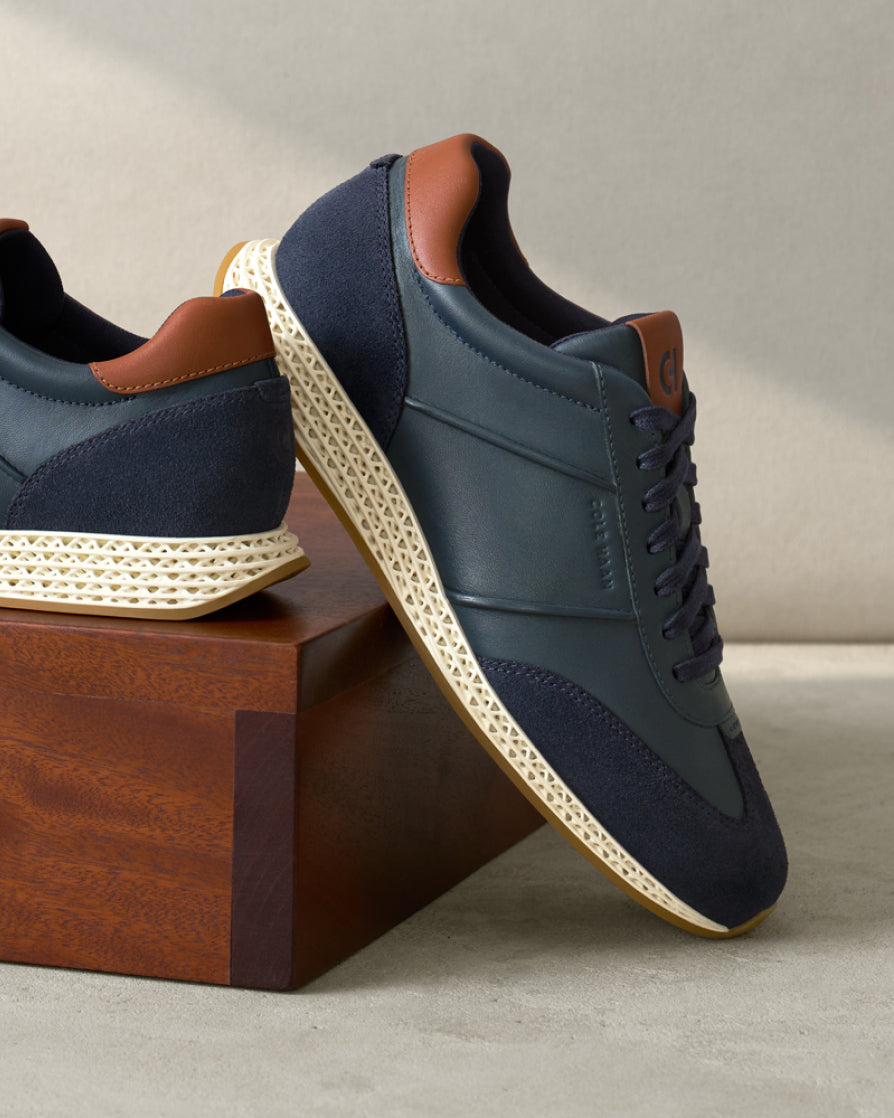 Navy sneakers with brown accents on a wooden block against a neutral background