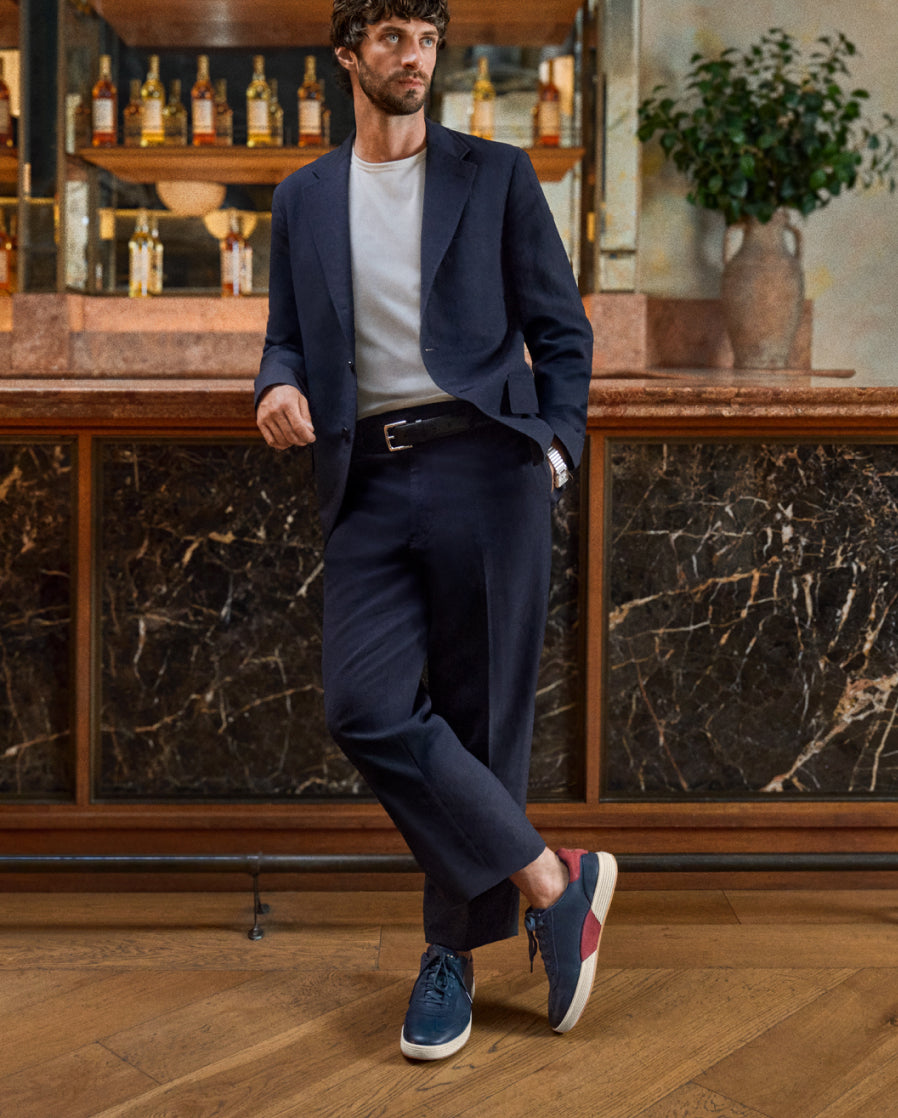 Man in a navy suit with blue sneakers standing in a bar setting