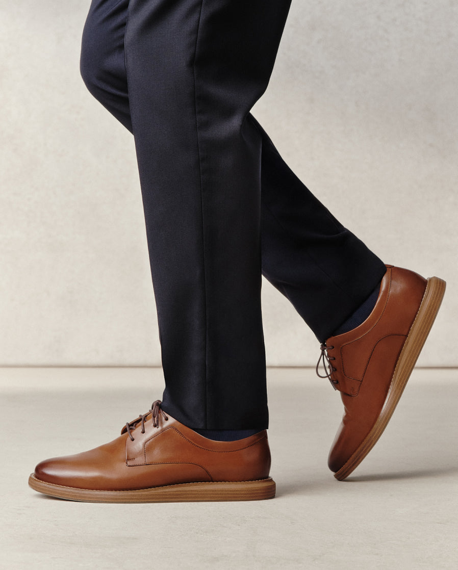 Brown leather shoes worn with black pants on a neutral background