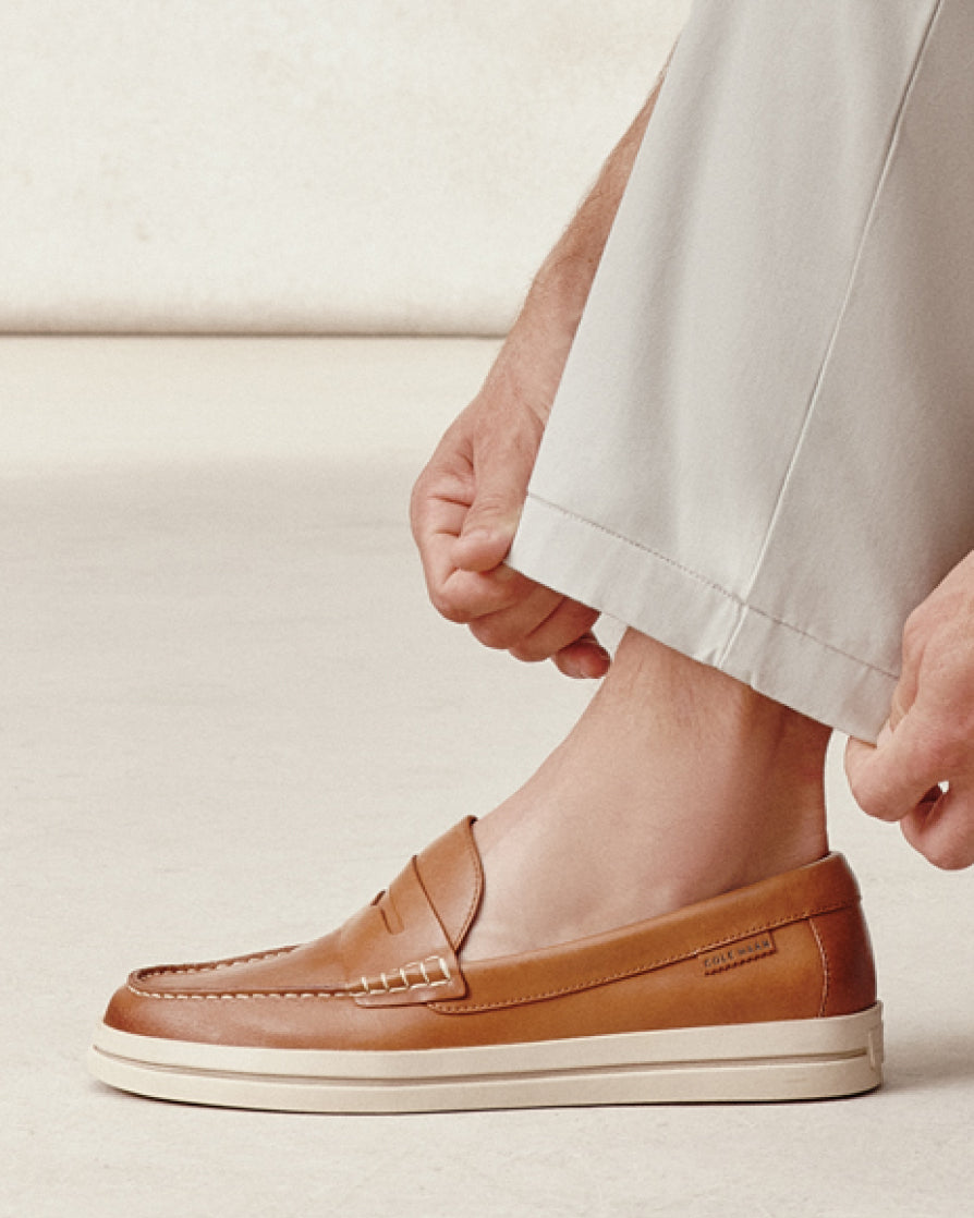 Brown leather shoe worn with light-colored pants on a neutral background