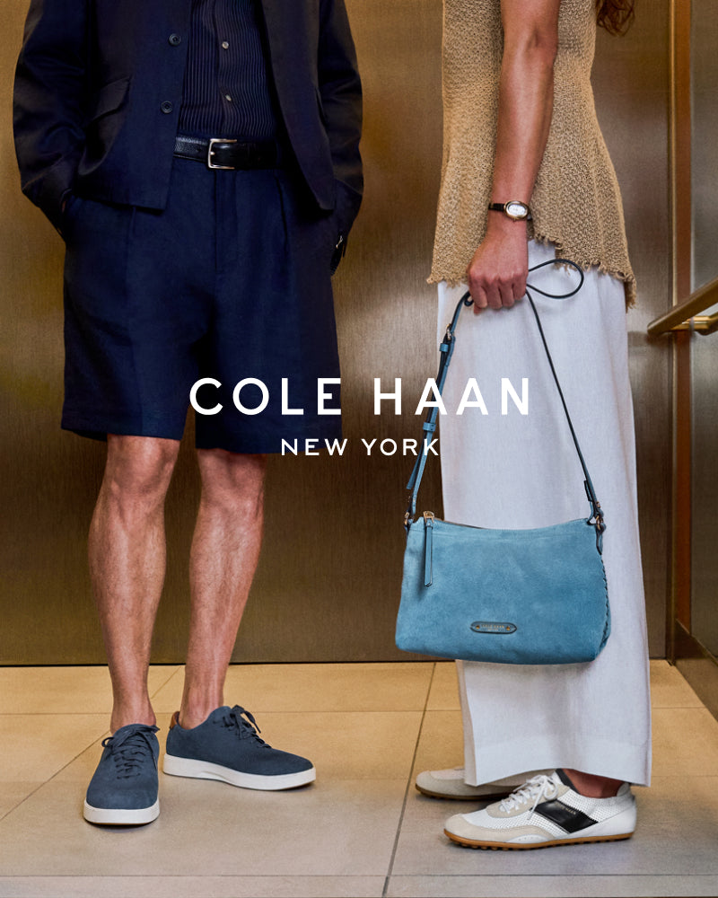 Two people wearing Cole Haan shoes with a blue handbag, standing indoors.