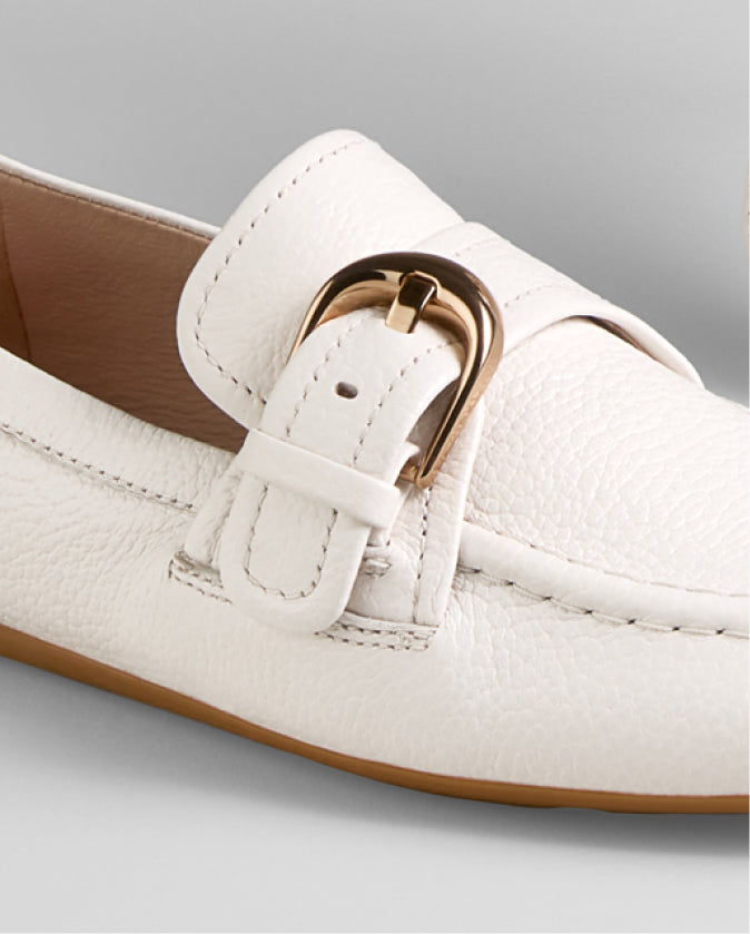 White loafer shoe with a gold buckle on a light gray background