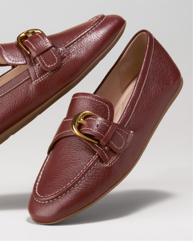 Pair of maroon loafers with gold buckles on a light gray background