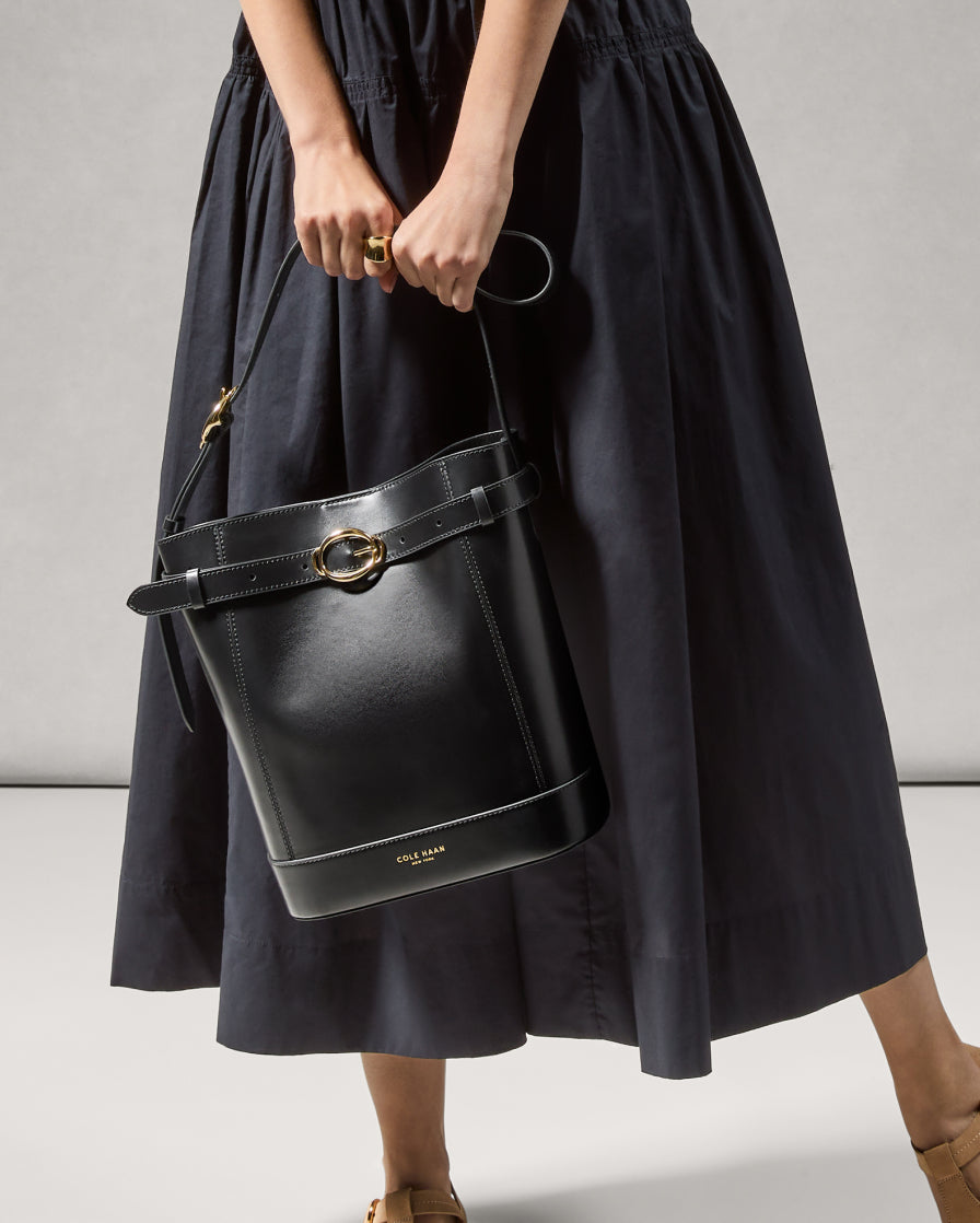 Person holding a black leather handbag with a gold clasp against a neutral background