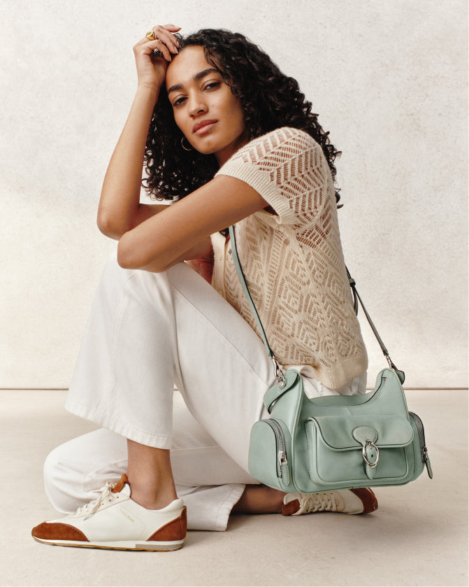 Woman sitting on a light-colored floor with a light green handbag