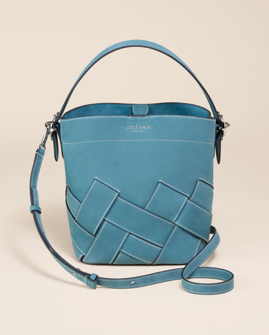 Teal leather handbag with woven strap on a beige background