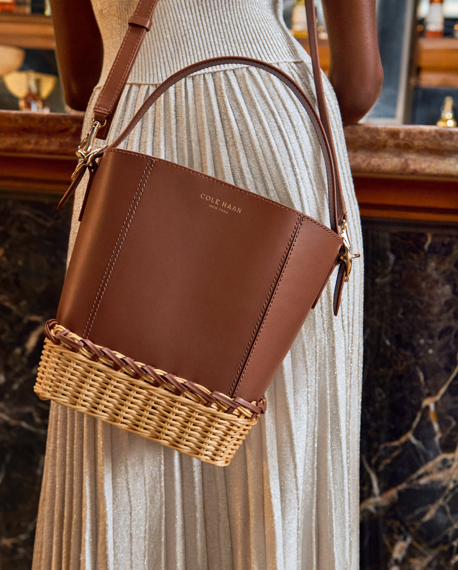 Brown leather handbag with wicker base held by a person in a light dress.