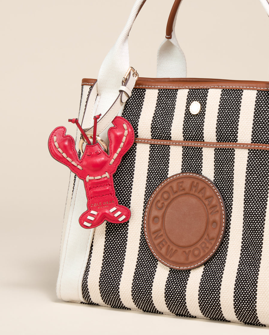 Striped handbag with a red lobster charm and Cole Haan logo.