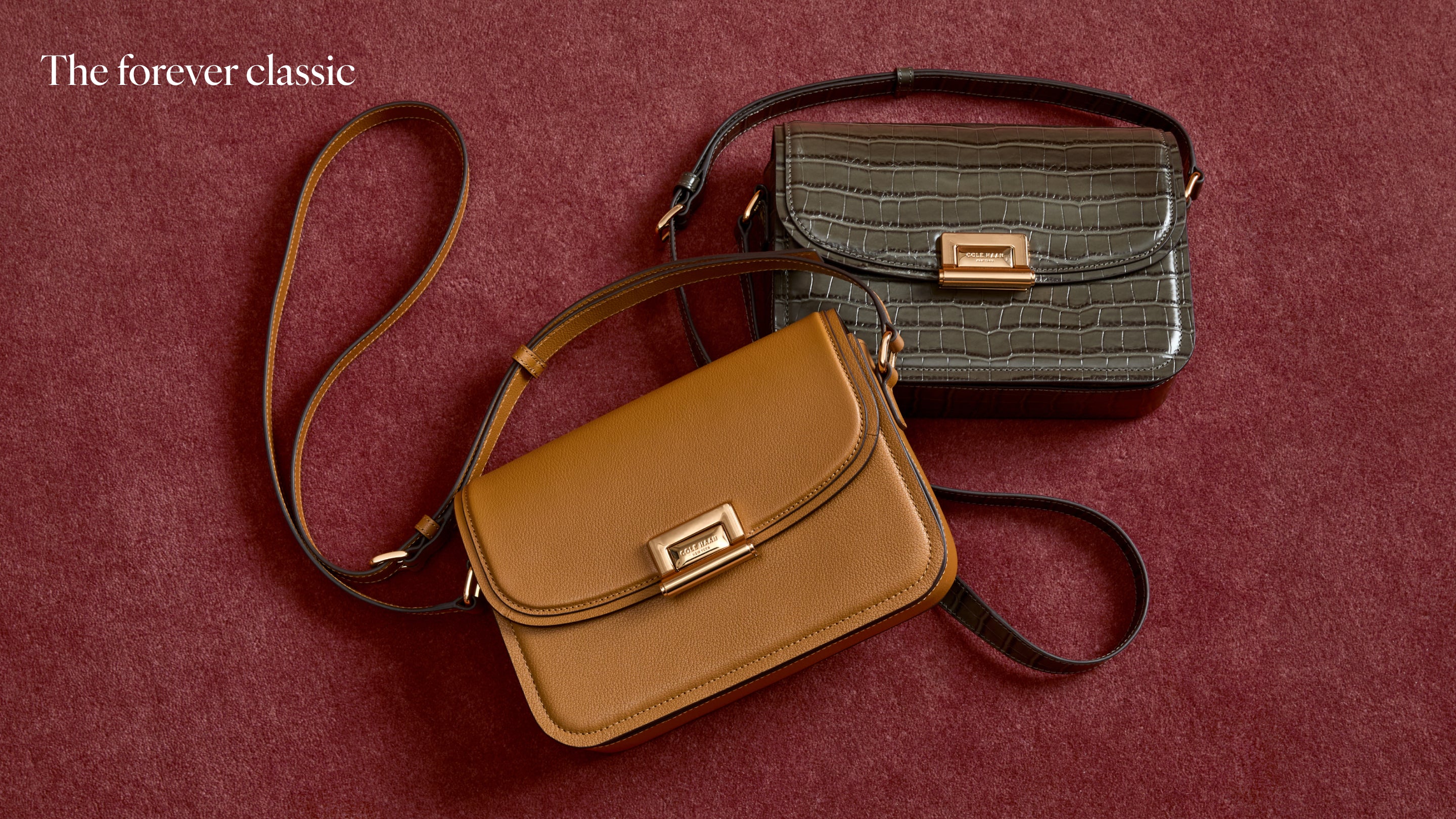 Two shoulder bags arranged on a textured burgundy background. The front bag is tan with a dark strap and gold-tone clasp, and the rear bag is dark brown with a crocodile-embossed texture and a gold clasp.