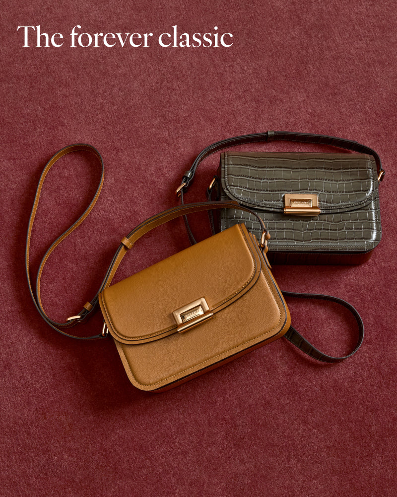 Two classic handbags on a textured burgundy background. The foreground bag is tan leather with a gold-tone clasp and a dark strap.