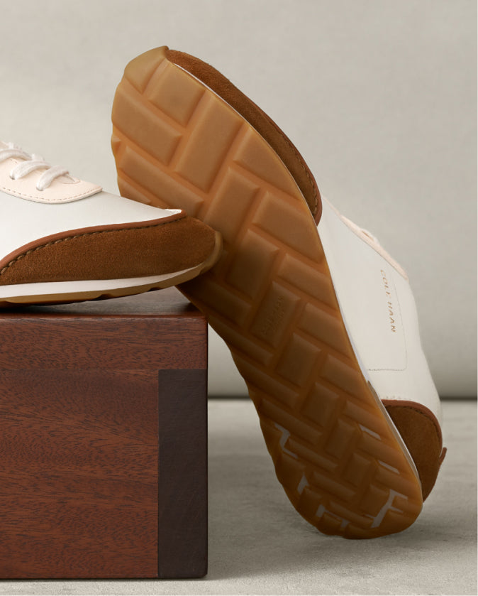Close-up of a shoe with a brown sole on a wooden block against a neutral background