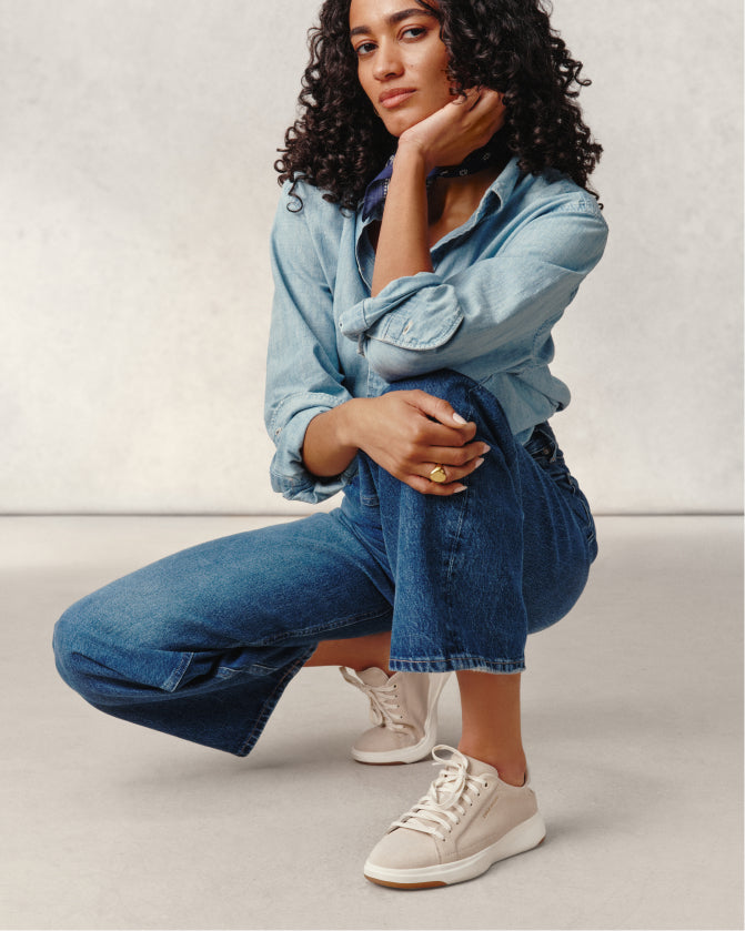 Woman wearing a denim outfit with beige sneakers on a plain background