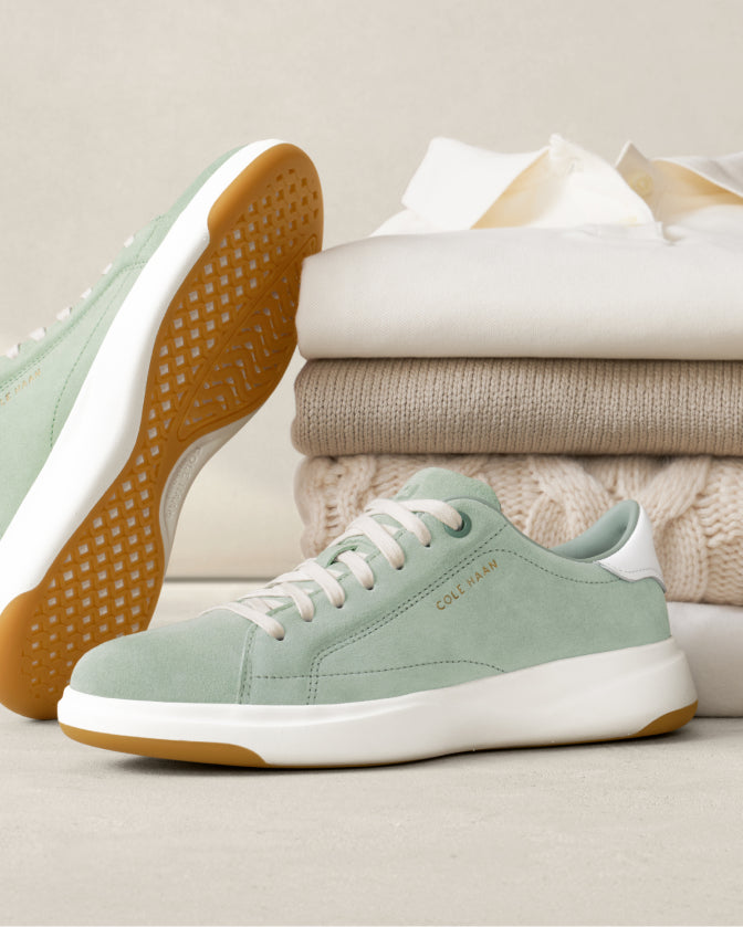 Green sneakers with white soles on a light surface with folded clothes in the background