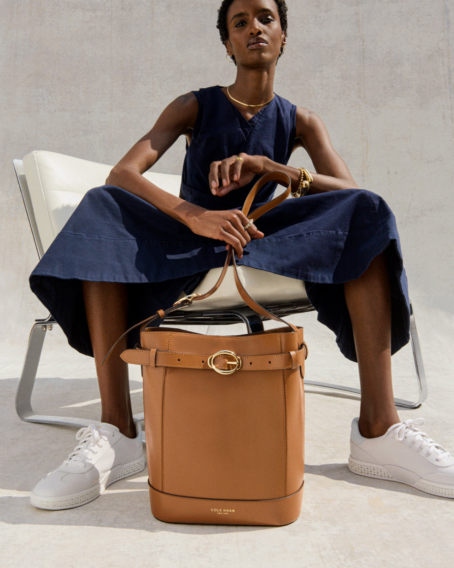Woman sitting on a chair holding a tan leather bucket bag with a neutral background