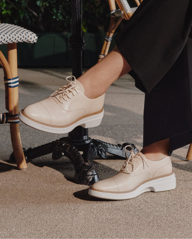 Person wearing beige leather shoes with white soles on a textured surface.