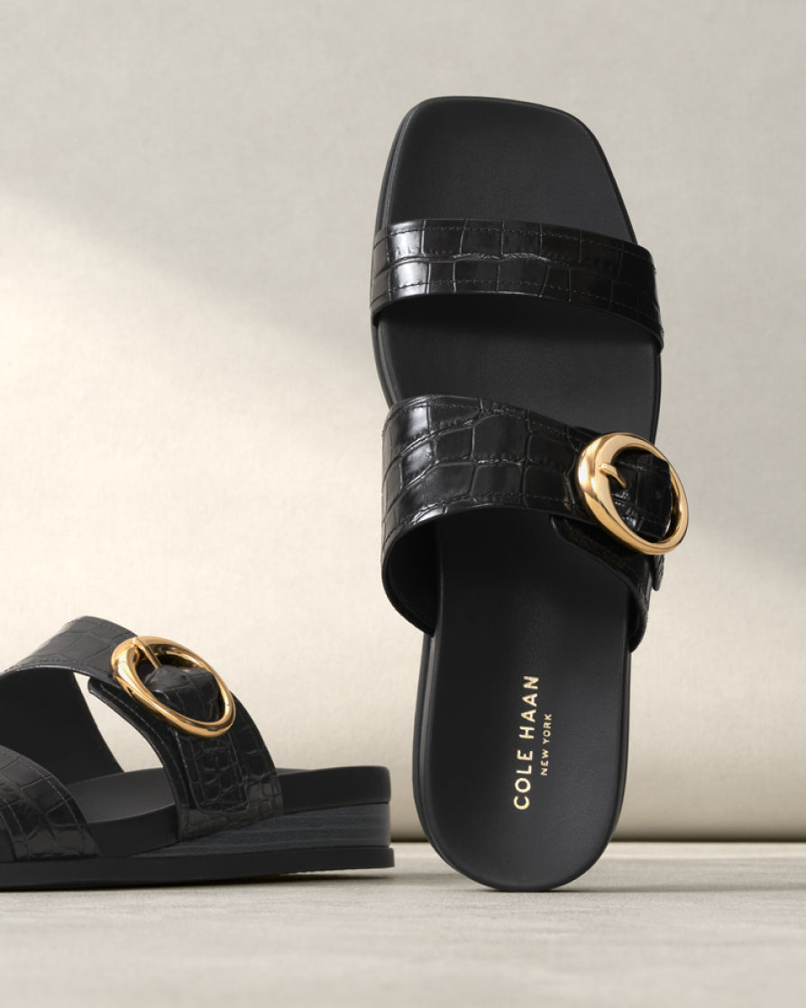 Black crocodile-patterned sandals with gold buckles on a light background