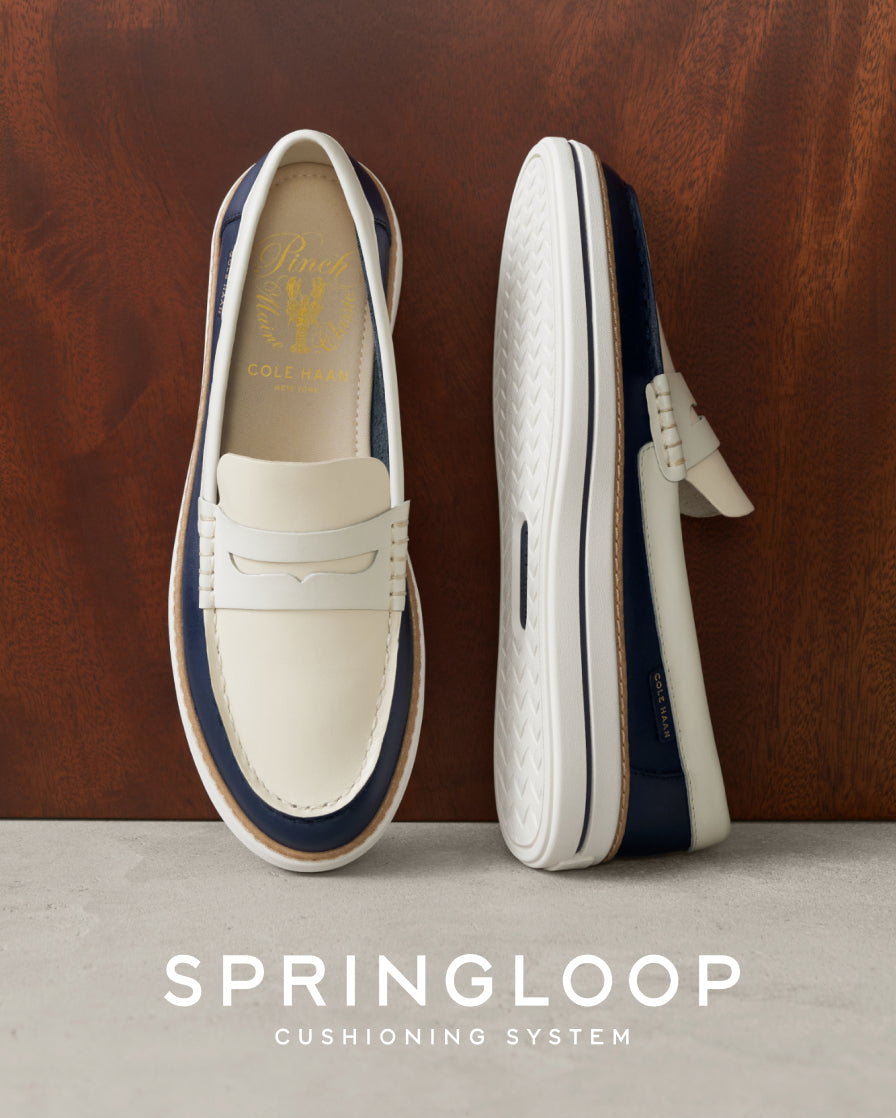White loafers with navy accents on a wooden background, featuring the Springloop cushioning system.