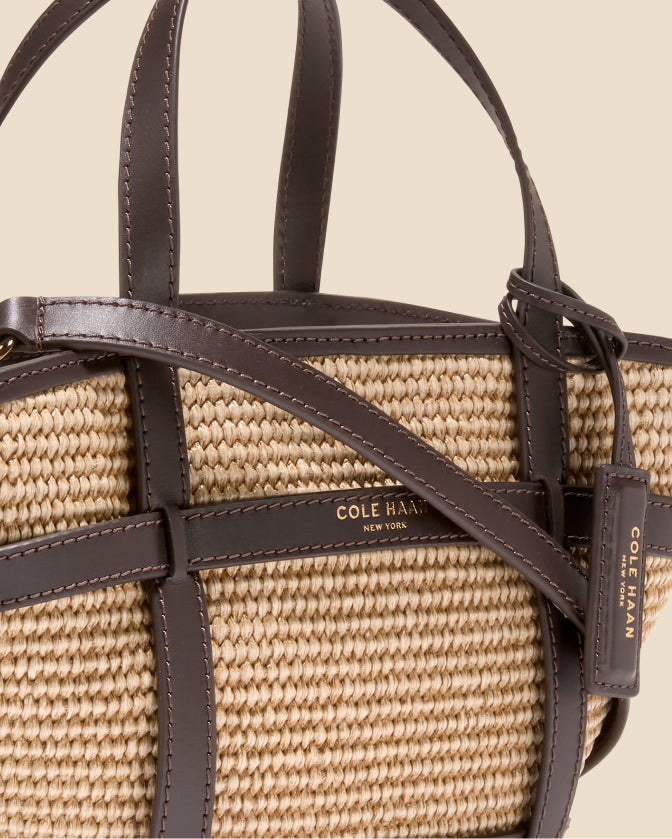 Close-up of a Cole Haan handbag with woven pattern and brown leather straps on a beige background.