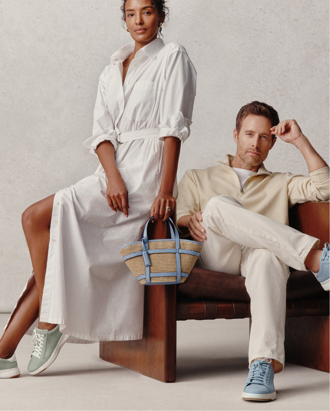 Two people sitting on a bench, one in a white dress holding a bag, the other in a beige outfit.