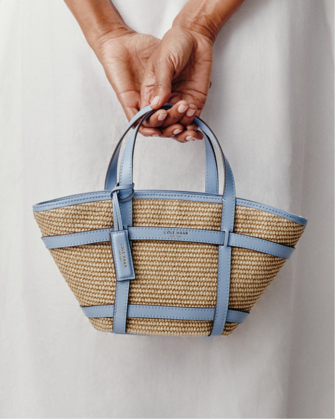 Woven basket with blue straps held by a person against a light background
