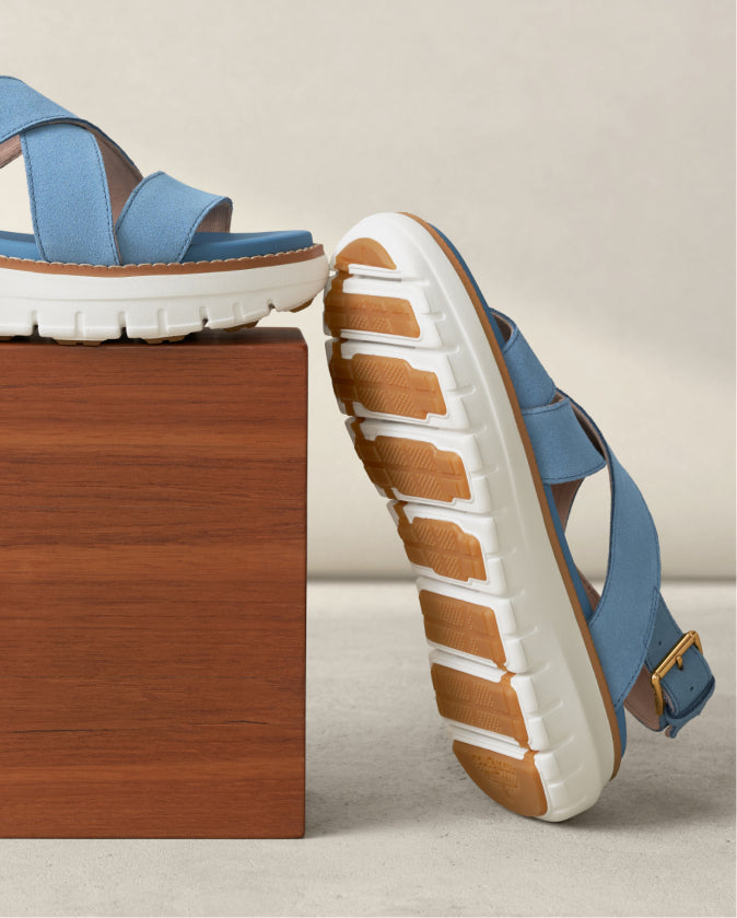 Blue sandals with brown soles on a wooden block against a beige background