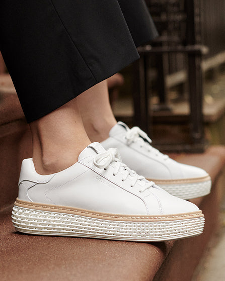 White sneakers with a white sole worn by a person sitting on a wooden bench.