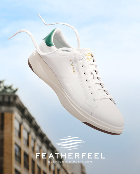 White sneaker with green accent on a blurred cityscape background, featuring the Featherfeel brand.