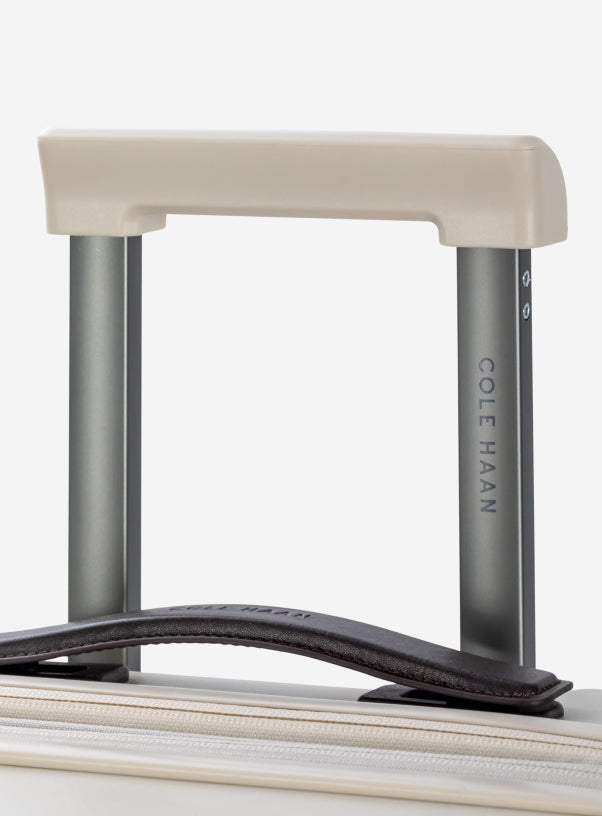 Close-up of a suitcase handle with 'Cole Haan' branding on a white background