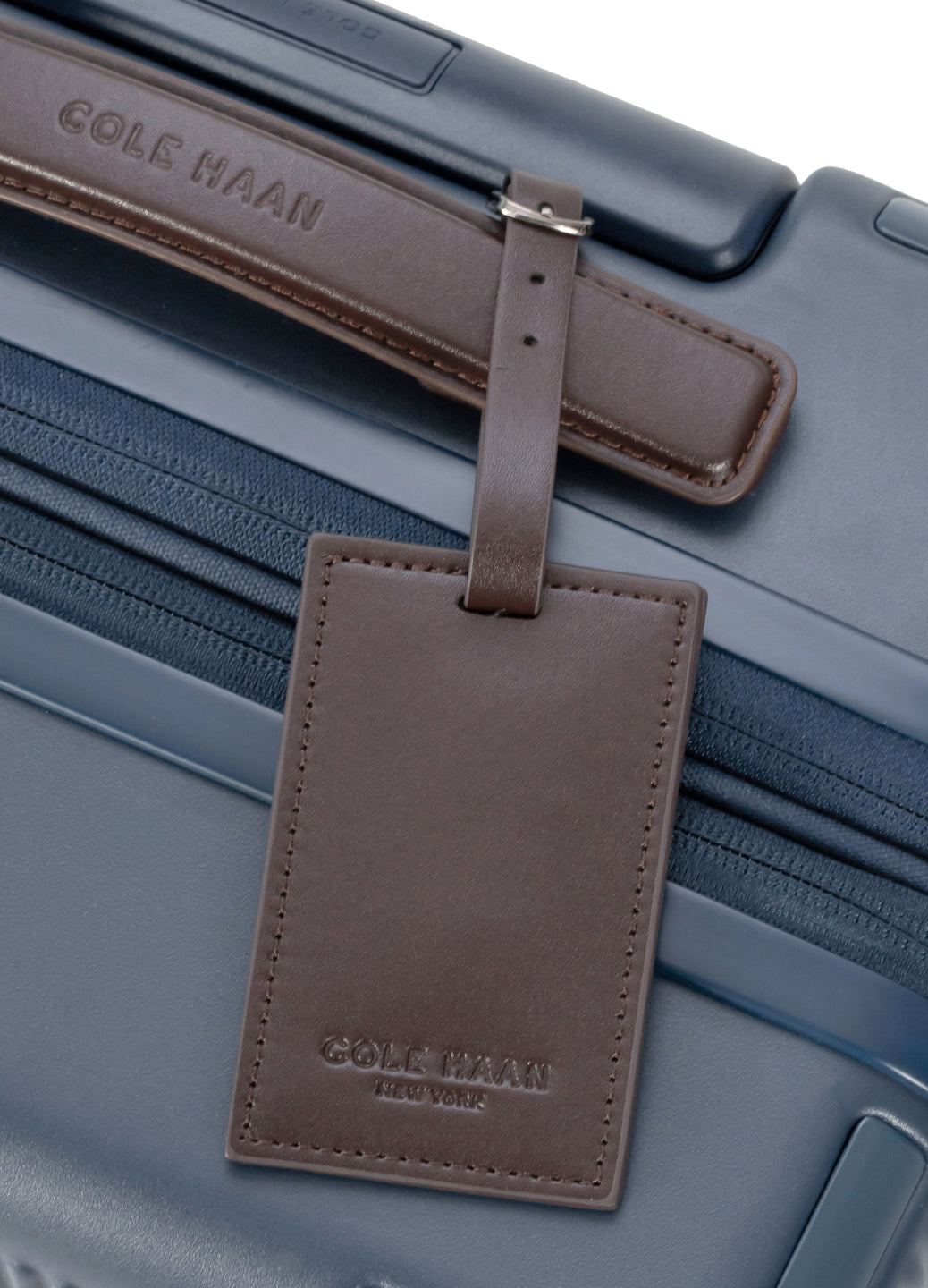 Brown leather luggage tag with 'Cole Haan' branding on a blue suitcase.