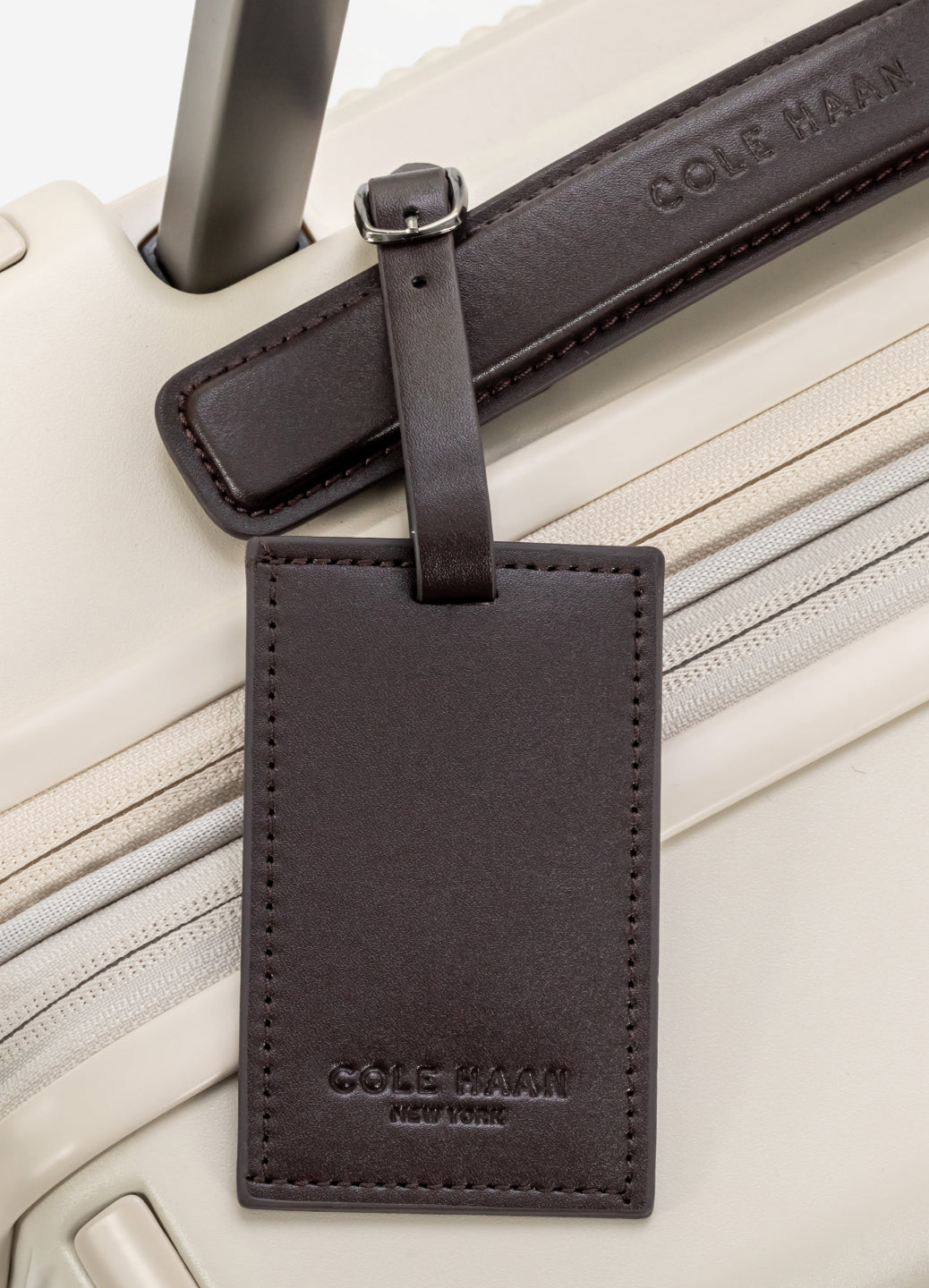 Black leather luggage tag on a Beige suitcase with 'Cole Haan' branding.