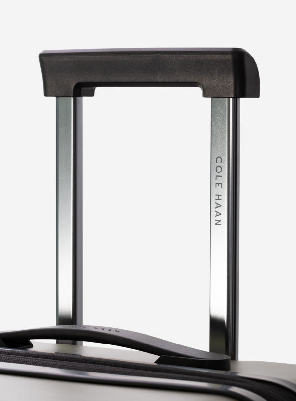 Close-up of a green suitcase handle with 'Cole Haan' branding on a white background