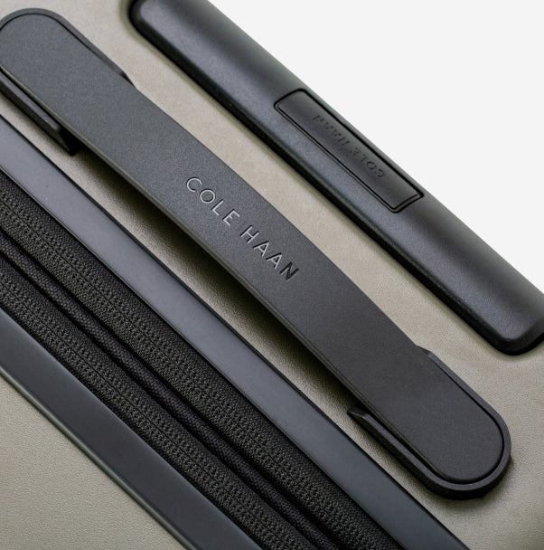 Close-up of a green Cole Haan suitcase with black handle and side panel.