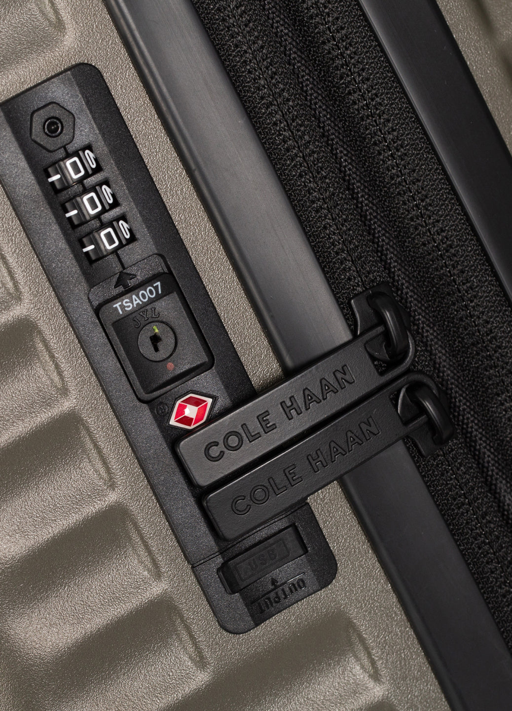 Close-up of a green suitcase handle with a combination lock and Cole Haan branding.