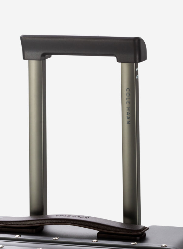 Close-up of a suitcase handle with 'Cole Haan' branding on a white background