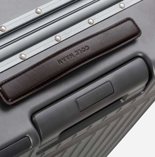 Close-up of a gray Cole Haan suitcase with a focus on the brand name.
