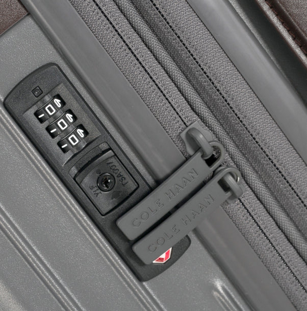 Close-up of a gray suitcase with a combination lock and Cole Haan branding.